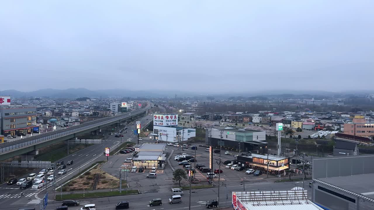 Aerial city view of Aomori Bay with roads, cars, shops, and a cloudy evening sky