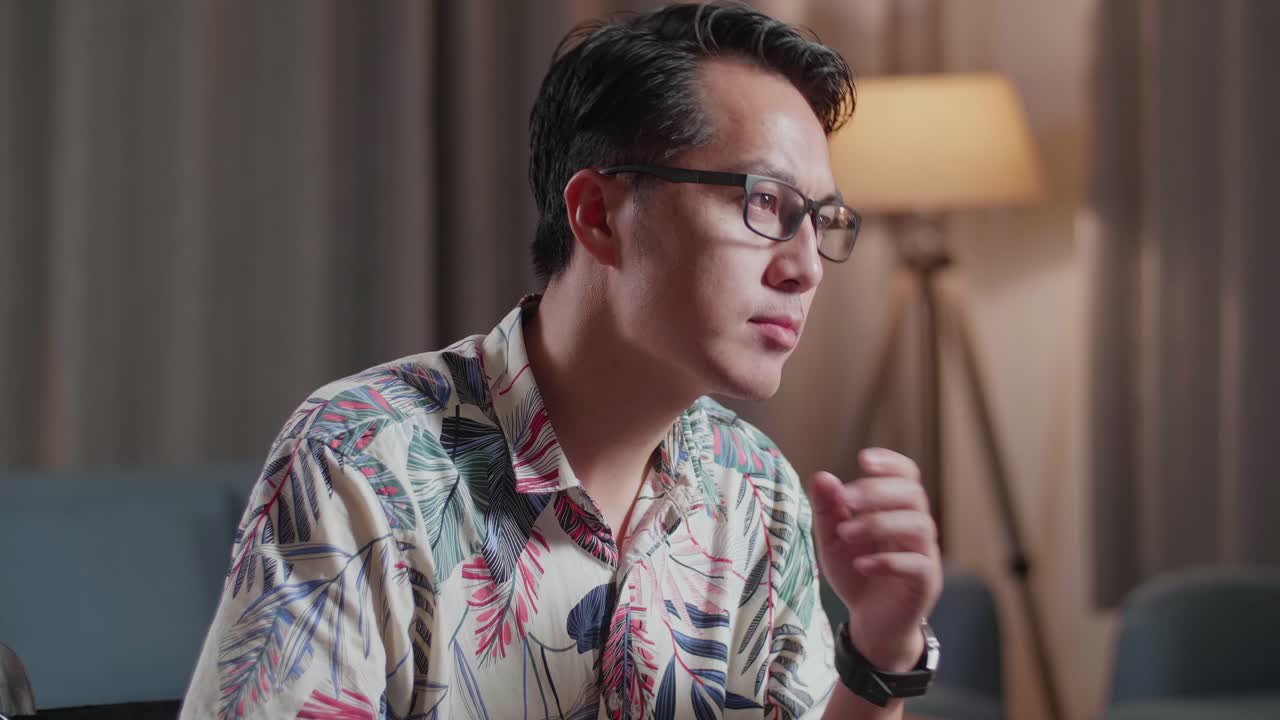 primer plano de un hombre asiático en silla de ruedas pensando en algo y levantando el dedo índice mientras edita el video por un escritorio al lado de la cámara en casa