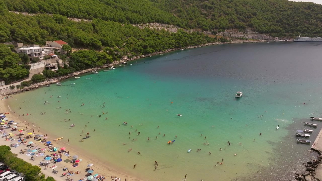 I vacanzieri riempiono la riva sabbiosa e i bassi fondali turchesi della baia di Prapratno, mentre barche e paddleboard punteggiano le acque più profonde dell'Adriatico