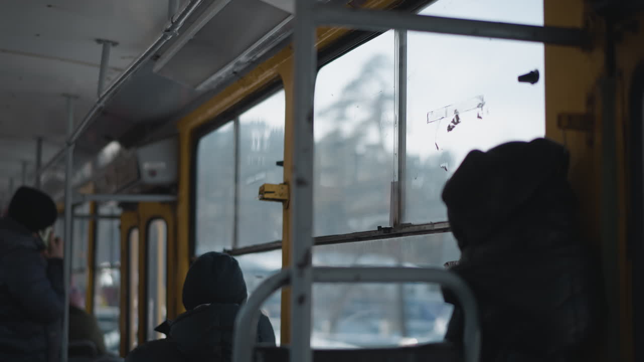 moving bus interior with passengers seated while empty rear seat near transparent windows, winter light filters through frosted glass showing snowy street and cars, calm commute mood with soft motion