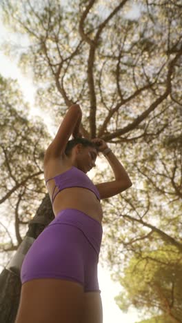 woman stretching outdoors in purple athletic wear under sunny trees