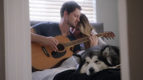 couple playing guitar with dog in bedroom