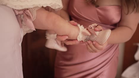 mother carefully putting on a white baby shoe with lace and ribbon, highlighting a loving and tender moment of care and preparation