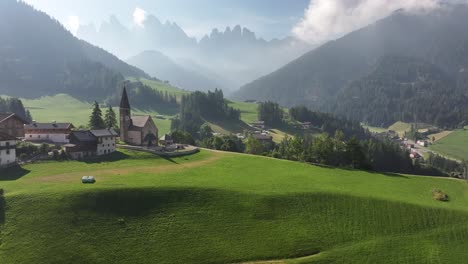 aerial of a quaint residential area situated against the dramatic mountain backdrop of chiesa di santa maddalena and drei zinnen in the dolomites, south tyrol, funes, italy