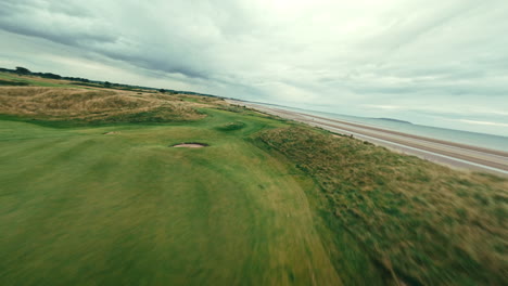 fpv flyover par 5 along the coastline of ireland links golf course, rolling green grass fairways and bunkers along the water