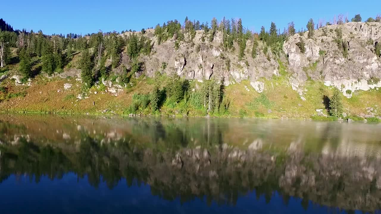 The mountains are reflected in the water of this mountain lake as steam raises