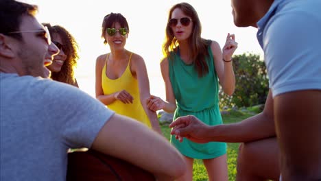 multi ethnic friends dancing to guitar on beach