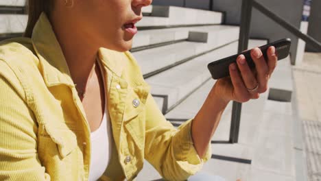 Feliz-Mujer-Caucásica-Sentada-En-Las-Escaleras,-Usando-Un-Teléfono-Inteligente-En-Un-Día-Soleado