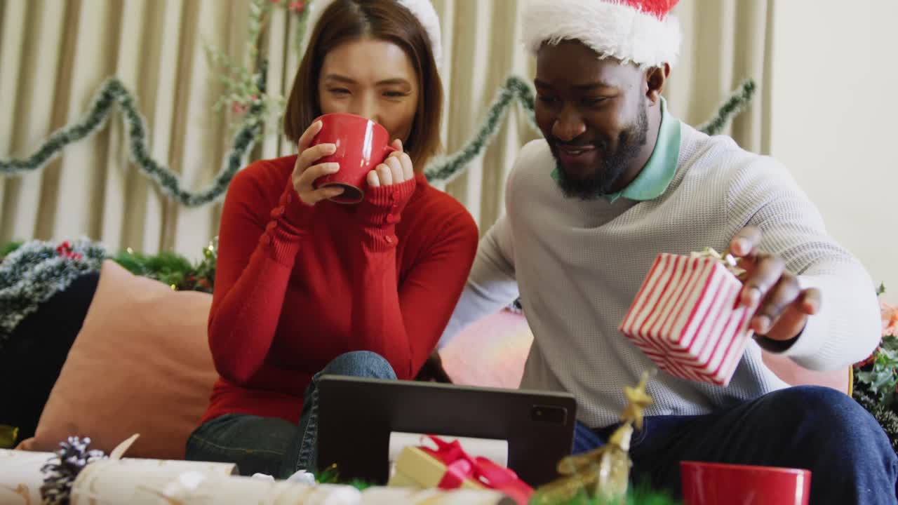 video de una feliz pareja diversa en sombreros de santa haciendo una llamada de video de computadora portátil de navidad en casa