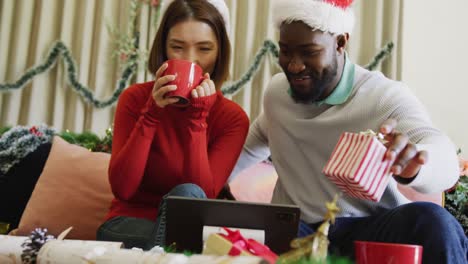 Video-De-Una-Feliz-Pareja-Diversa-Con-Gorros-De-Papá-Noel-Haciendo-Una-Videollamada-Navideña-Con-Una-Computadora-Portátil-En-Casa