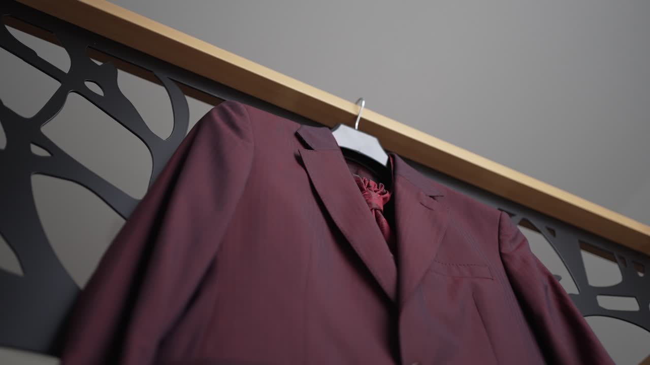 Low angle view of a burgundy suit on a hanger, displayed against a contemporary black and wooden design