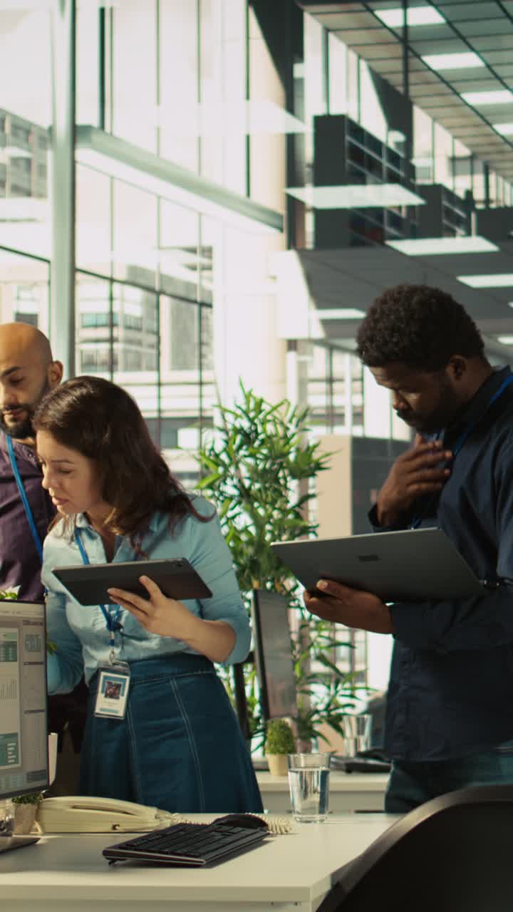Vertical video Multiethnic coworkers looking over revenue figures on tablet in diverse office