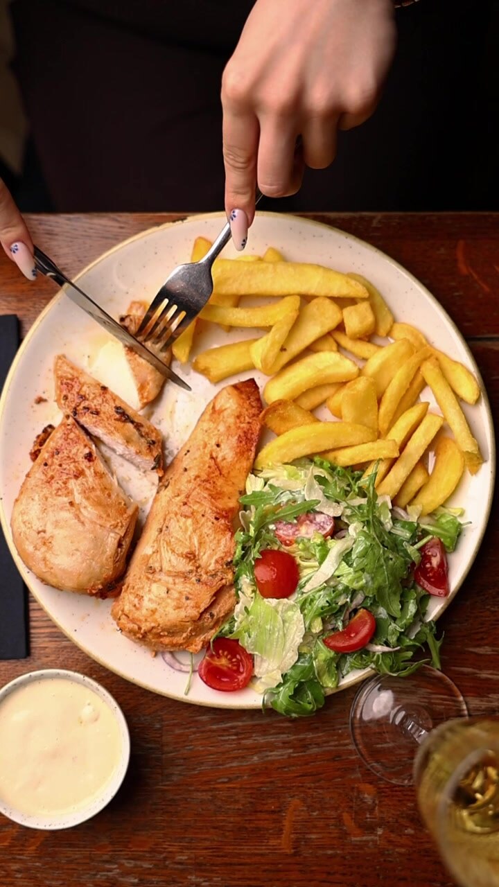 Persona cortando pollo a la parrilla con patatas fritas y ensalada