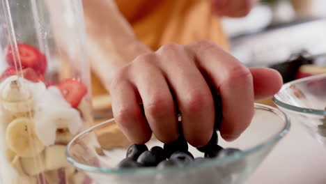 la mano de un hombre biracial haciendo batido poniendo frutas cortadas en la licuadora, copia el espacio, cámara lenta