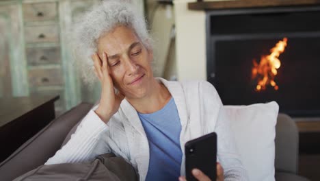 Senior-mixed-race-woman-sitting-on-sofa-using-smartphone