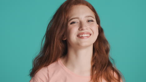 redheaded girl in front of camera on turquoise background.