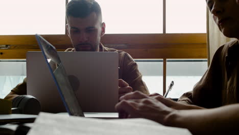 camera focuses on a boy of a study group using laptop, while other classmates write on paper and using the computer