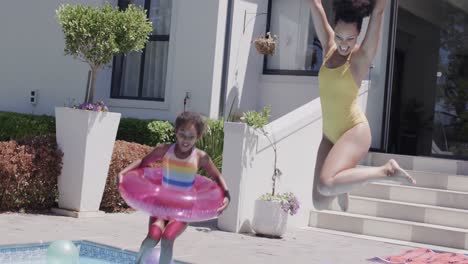 happy african american mother and daughter jumping into swimming pool, slow motion