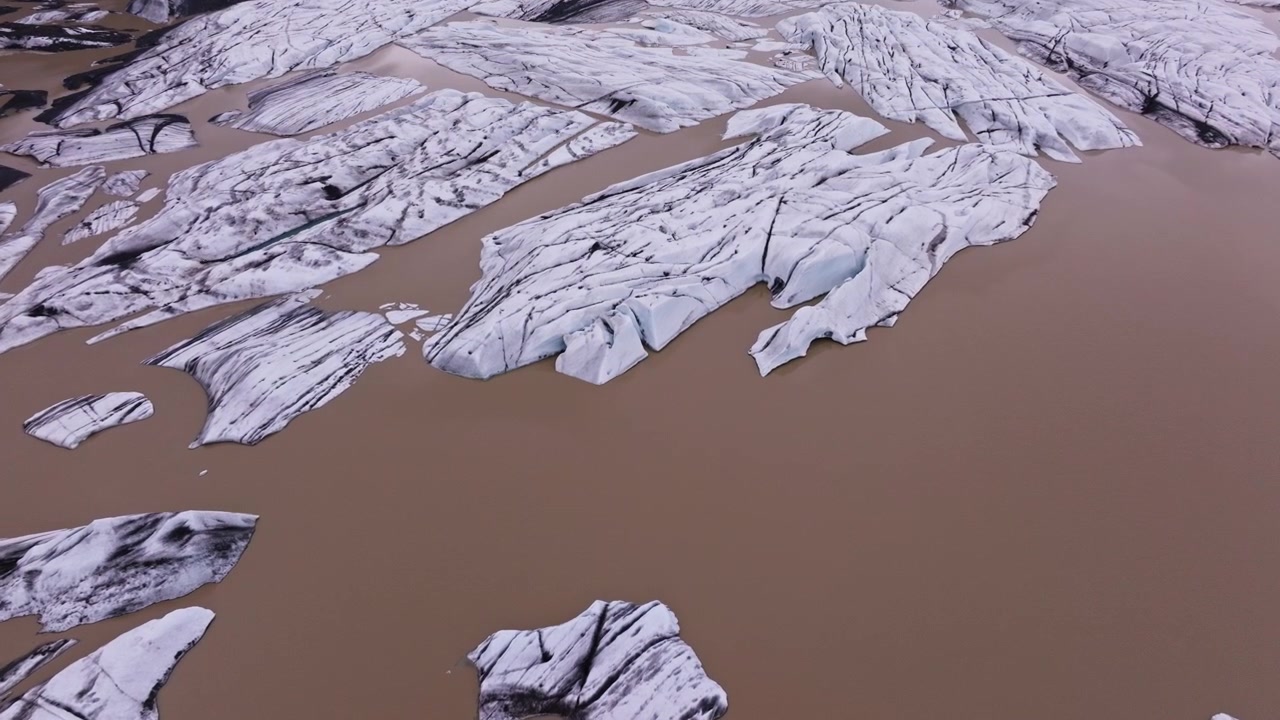 Silty brown waters of Iceland glacier lagoon with icebergs calving away. Aerial