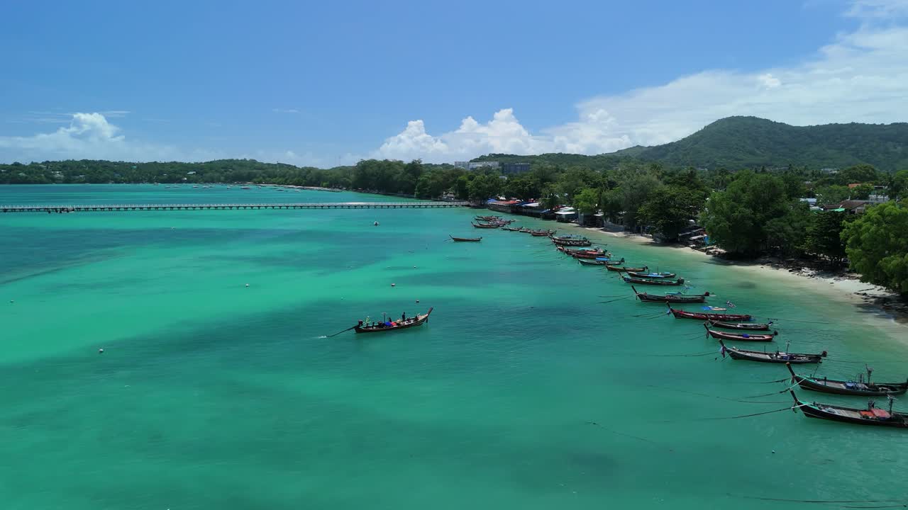 Drone follows a longtail boat toward the shoreline along turquoise Rawai Beach