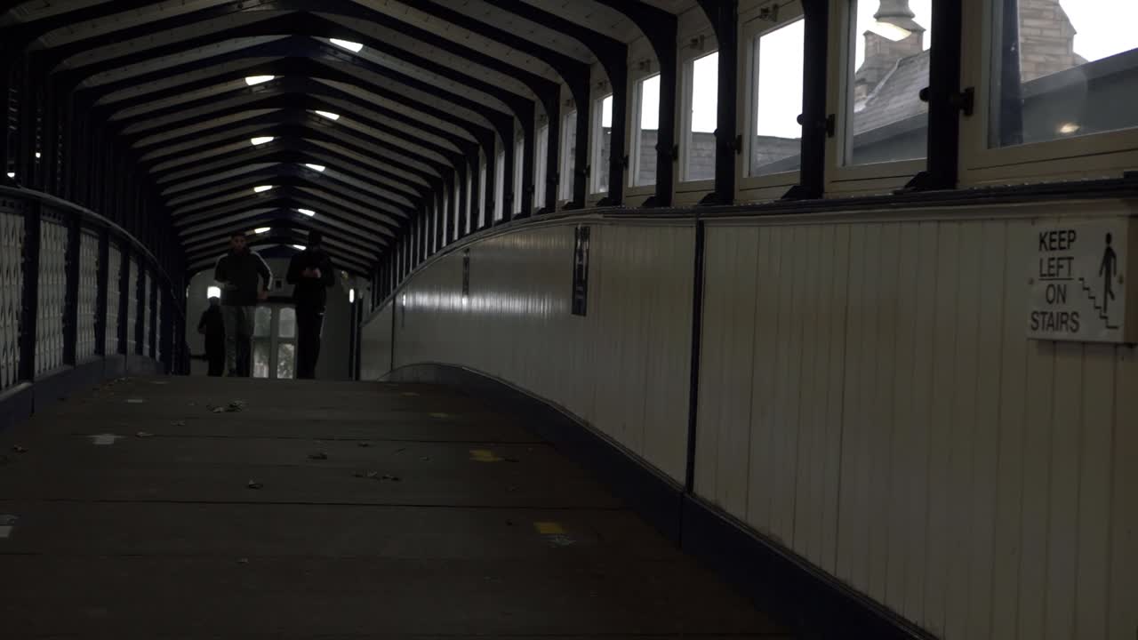 People in distance walking along dark railway bridge wide shot
