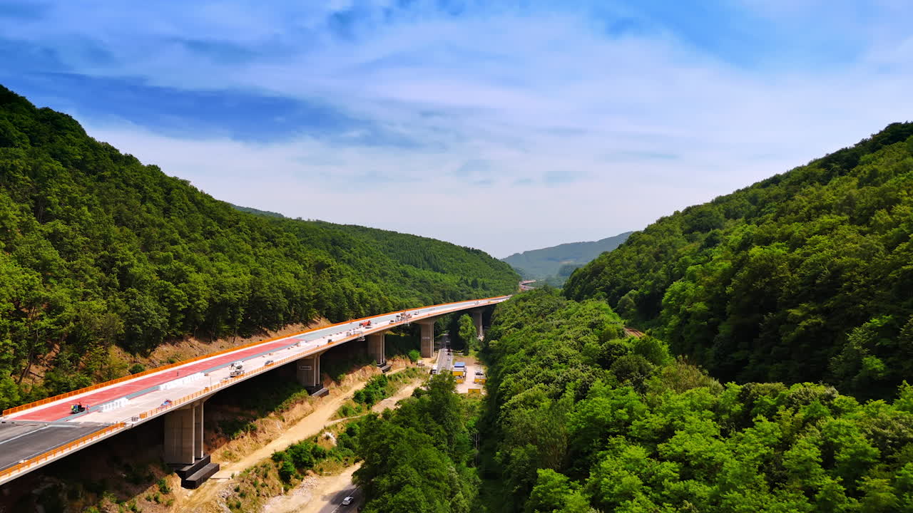 Striking new freeway being constructed in the green mountains. Rise over the rocky landscape revealing view on the road construction