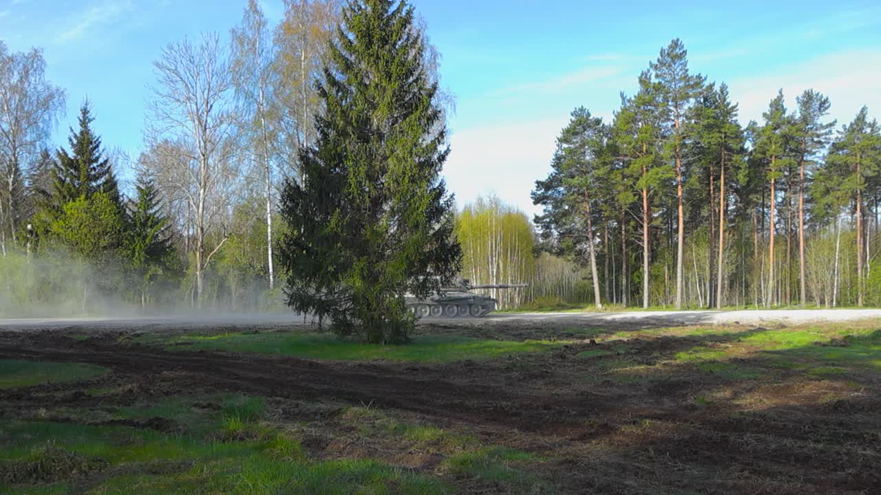 Gorgeous vibrant video of a British Challenger 2 4034 armored tank with a large cannon driving on a dusty forest gravel road fast making dust clouds behind it during a sunny summer day.