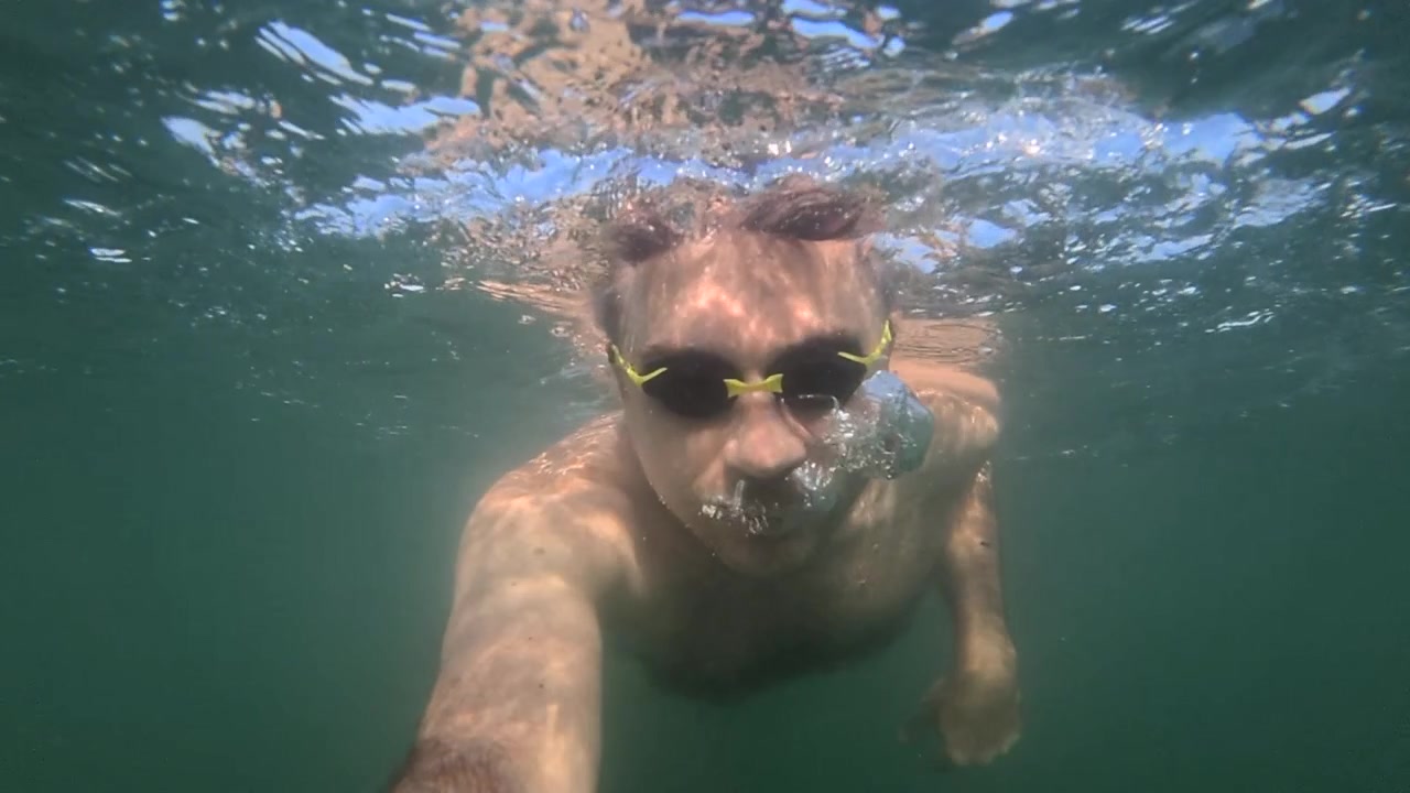 Uomo che nuota sott'acqua in acqua blu limpida, creando bolle e godendosi un'attività estiva rinfrescante.