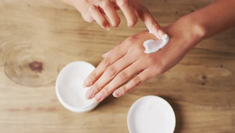 video of hands of caucasian woman moisturizing hands with cream on wooden surface