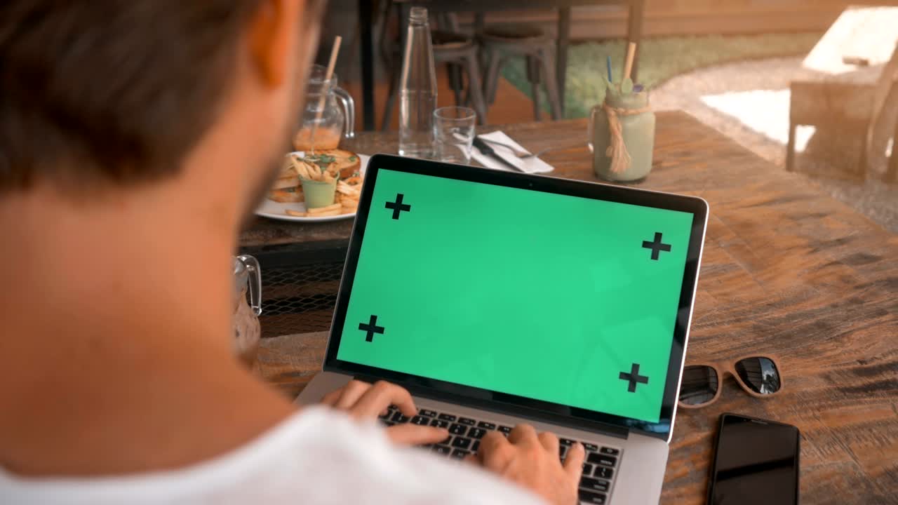 closeup de manos masculinas trabajando en una computadora portátil con pantalla verde en una cafetería