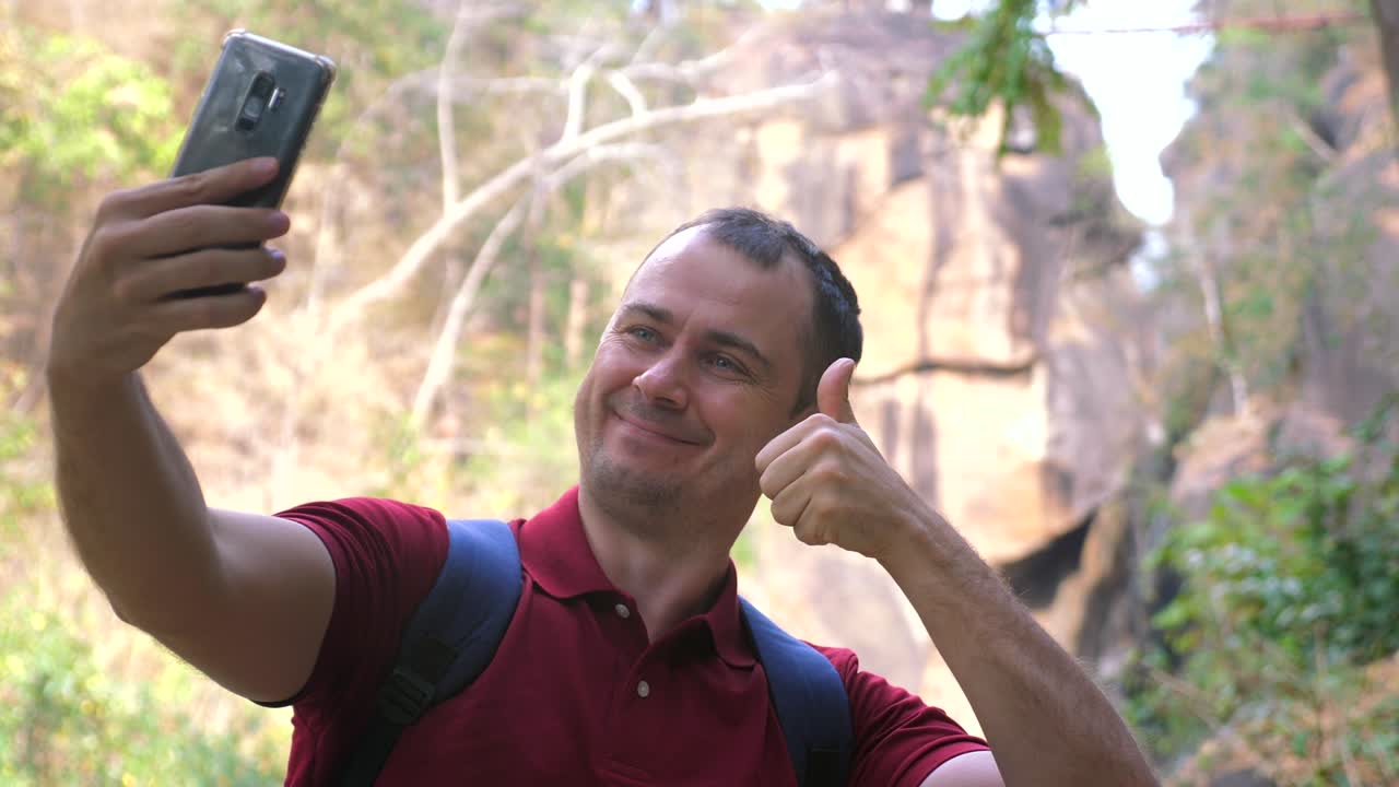 un viajero hombre sonriente toma selfies en su teléfono contra un cañón en un parque forestal. un hombre feliz excursionista graba video o toma fotos en la cámara con cañones de montaña y río contra el fondo del bosque