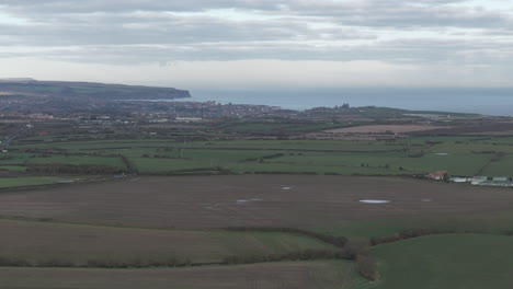 Luftaufnahme-Von-Feldern-Mit-Whitby-In-Der-Ferne-An-Der-Küste