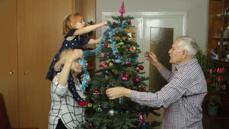 Children-girl-with-elderly-couple-grandparents-decorating-artificial-Christmas-pine-tree-at-home