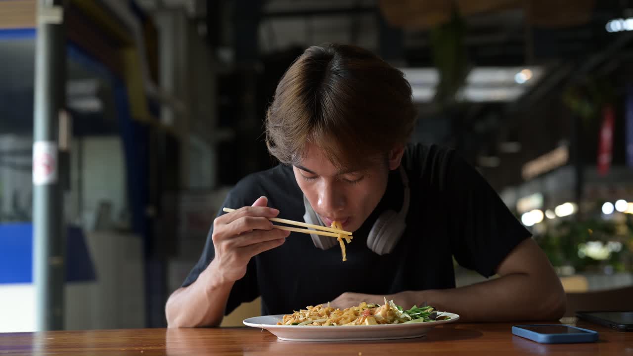 Pad Thai noodles eaten with chopsticks in Thailand by young tourist man during day. Famous street food cuisine loved by tourist and locals in Asia
