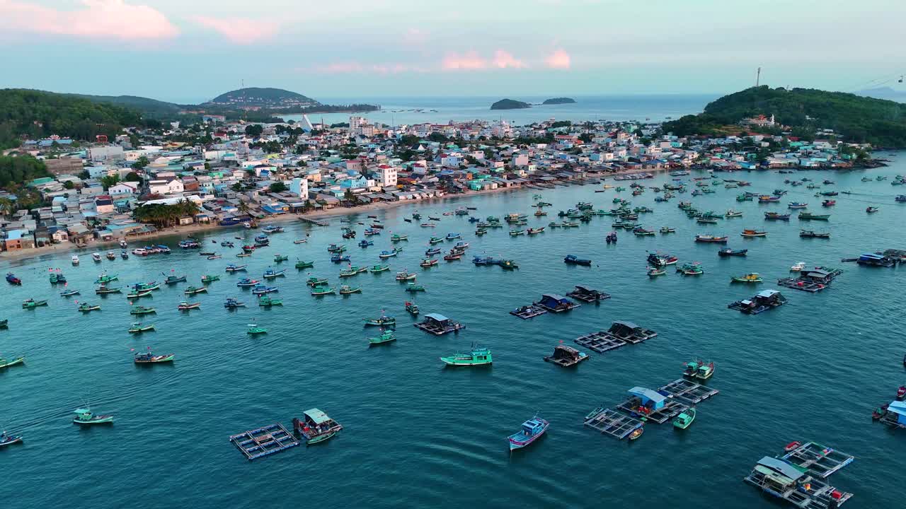 Drone shot of Phu Quoc Island during sunset. A fishing village with numerous fishing boats in the water and a cable car station visible on the horizon. Vietnam
