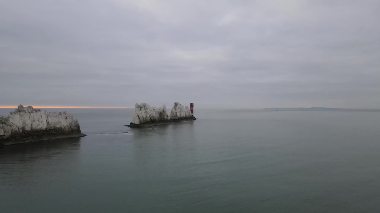 Volo di drone aereo 4K 30FPS lungo la scogliera bianca di The Needles nell'Isola di Wight, dirigendosi verso un faro rosso e bianco dove le onde si infrangono contro le rocce sottostanti.