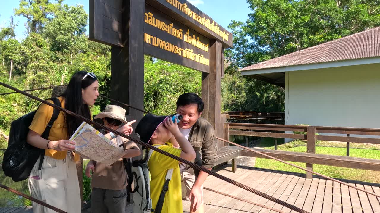 タイ人家族が地図と双眼鏡を使いながら、熱帯雨林の橋を一緒に探索しています。