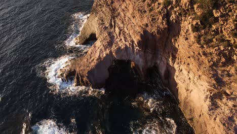 Aerial-view-of-remote-rugged-cliff-coastline,-open-arched-cave,-rising