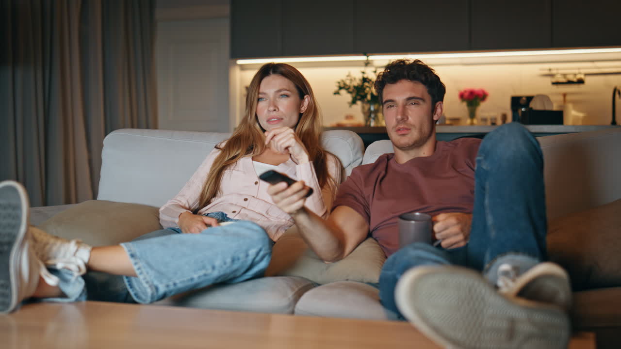 Giovane coppia che guarda la televisione cambiando canale sul divano. Coppia che sceglie un film.