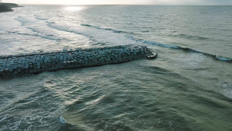 Aerial-establishing-view-of-protective-pier-with-concrete-blocks-and-rocks-at-Baltic-sea-coastline-at-Liepaja,-Latvia,-strengthening-beach-against-coastal-erosion,-drone-shot-moving-forward-tilt-down