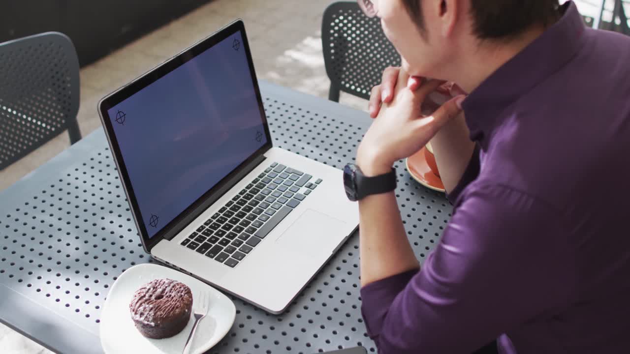 hombre asiático mirando la computadora portátil con espacio de copia mientras está sentado en una cafetería
