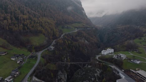 Calm-backwards-upwards-tilting-aerial-drone-view-of-Swiss-valley-with-pine-forests-and-clouds-on-moody-winter-day