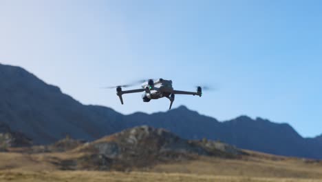 drone desce para pousar em um campo gramado com montanhas ao fundo