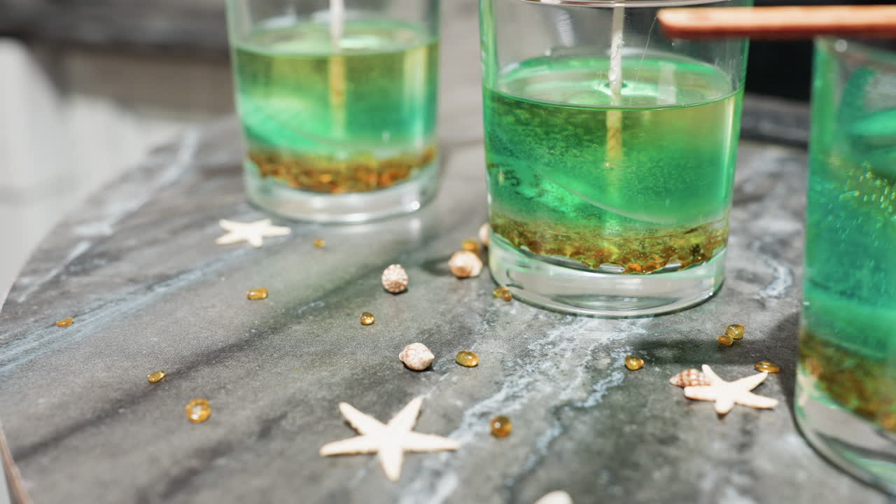 Female creative pours small shell-shaped, star-like, and round colorful decorative items from palms onto surface beside glass jars filled with green and gold cake mixture