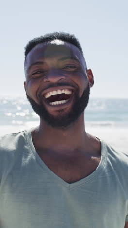 vertical video of happy african american man on beach smiling at camera