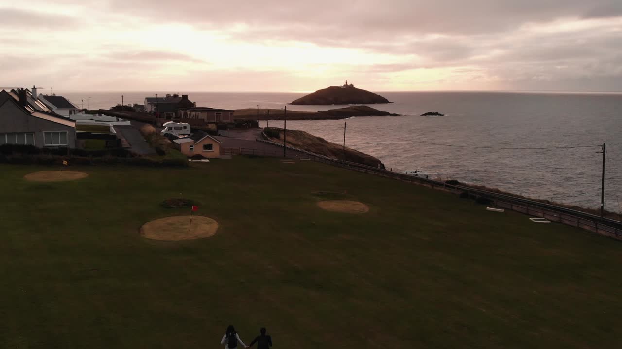 무명 여행 부부는 해가 지면 바다 위의 언덕에서 달리고 있습니다.