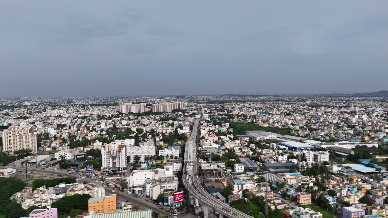 Vista ad angolo elevato della zona di Chennai Kattupakkam dove una nuova sopraelevata linea della metropolitana e la costruzione di un cavalcavia dominano la strada principale, attraversando una fitta griglia di case residenziali colorate