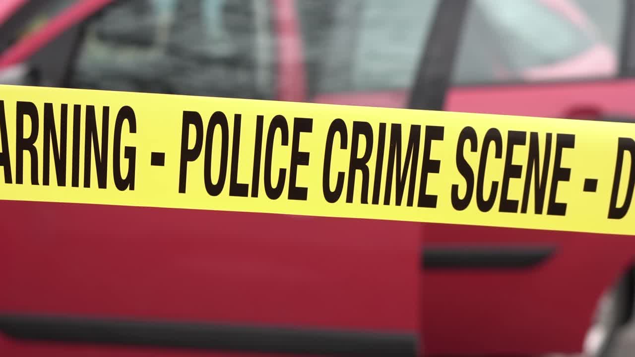 Police Crime Scene Tape RIbbon in Front of Red Car WIth Open Doors, Close Up