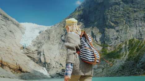 A-Woman-In-Warm-Clothes-Admires-The-Glacier-High-In-The-Mountains-Briksdal-Glacier-In-Norway-A-Trip-