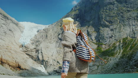 a woman in warm clothes admires the glacier high in the mountains briksdal glacier in norway a trip